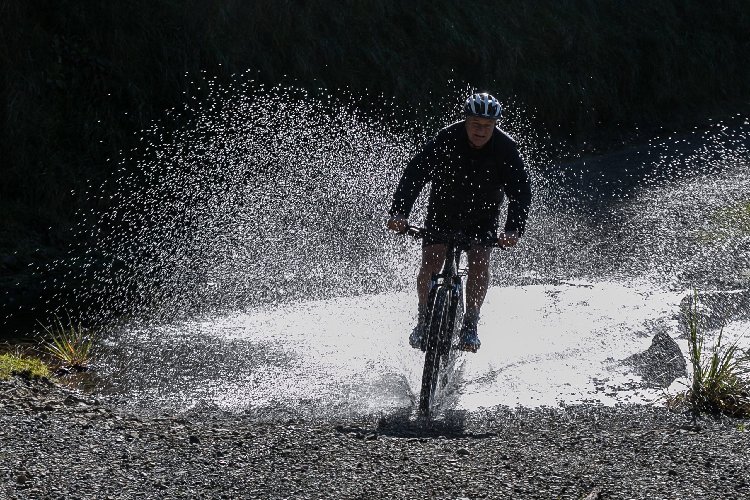 A cyclist splashing through a creek on the Remutaka Cycle Trail