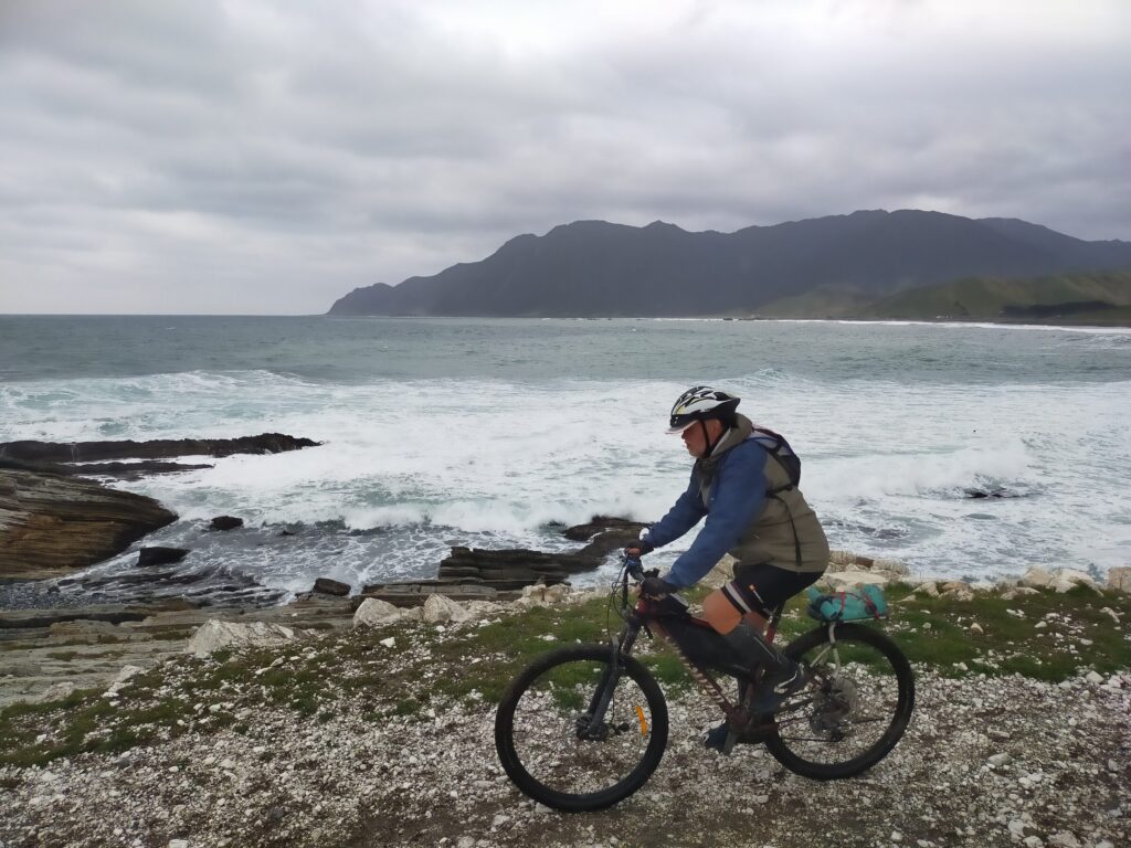 A rider on the gravel coast with surf breaking beside the track