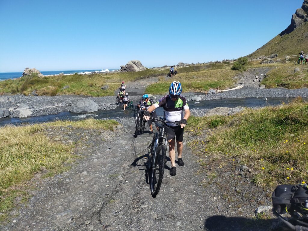 Riders pushing bikes through the Waitutuma stream